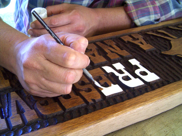 Mão pintando letras de uma placa entalhada